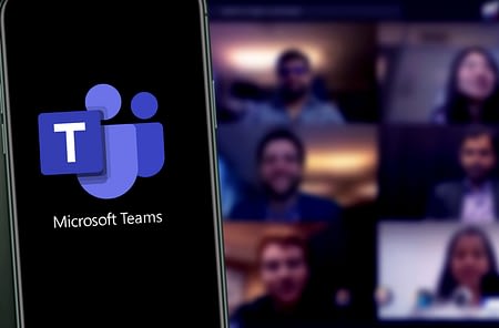 Microsoft Teams Logo on Phone and Microsoft Teams Meeting on Computer in Background
